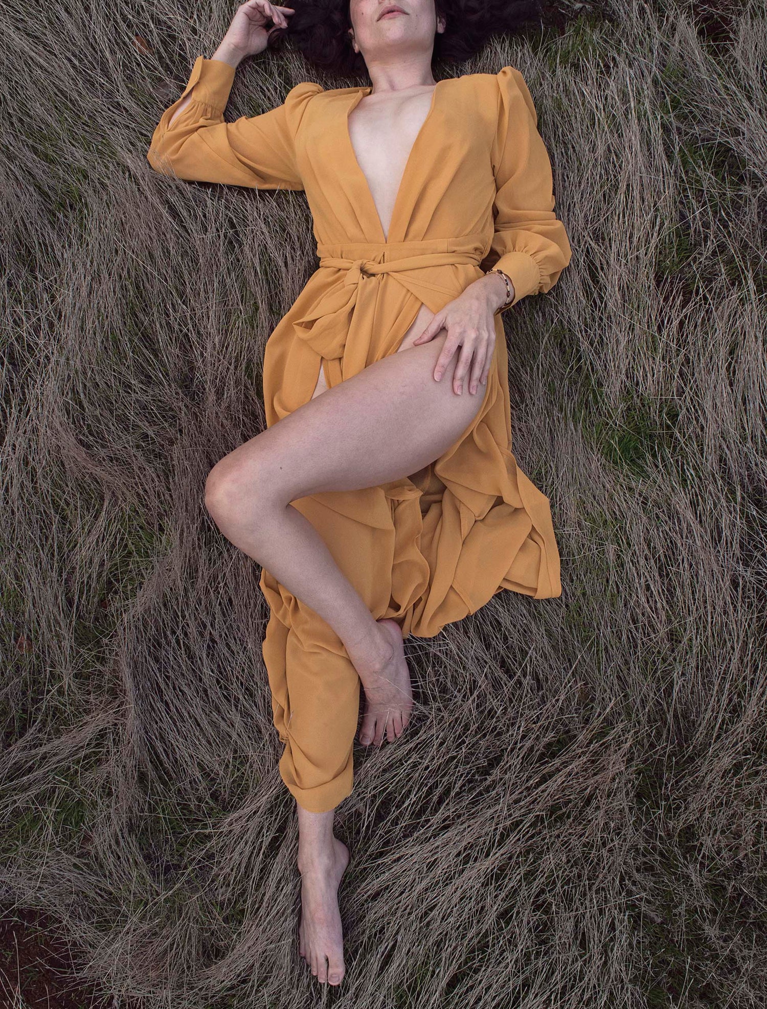 Xan from Stories of Evermore lays in the silver grass of a grassy knoll in a delicate mustard yellow gown.