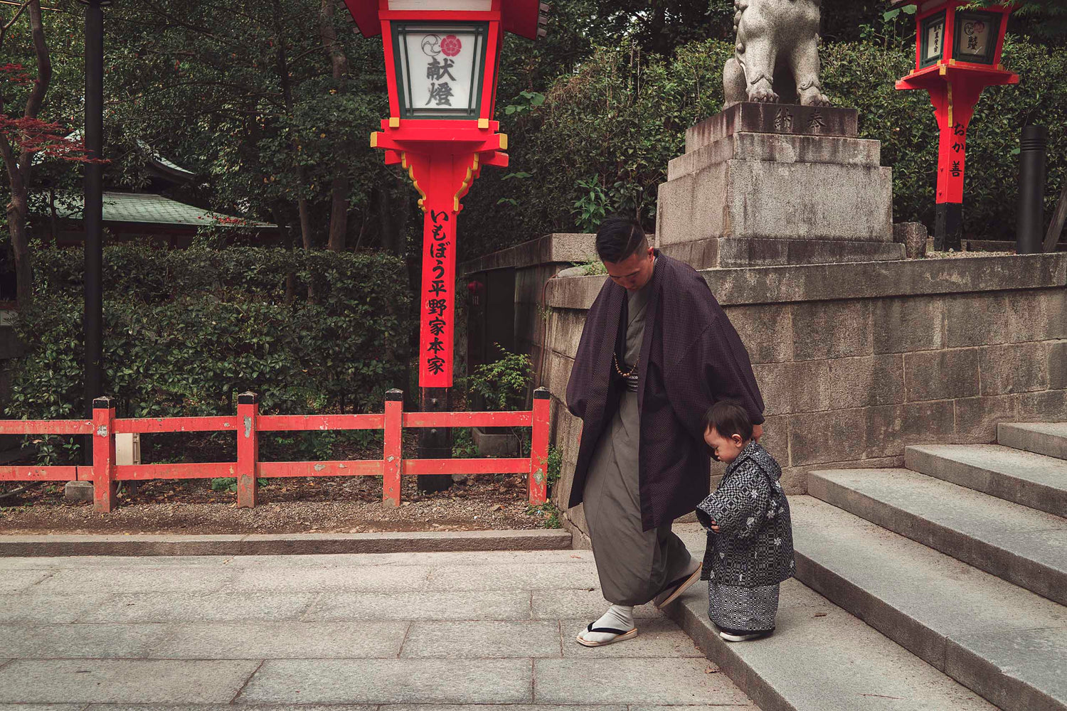 A young father escorts his youngest son down the temple steps in traditional Japanese kimono dress during a cherry blossom festival.