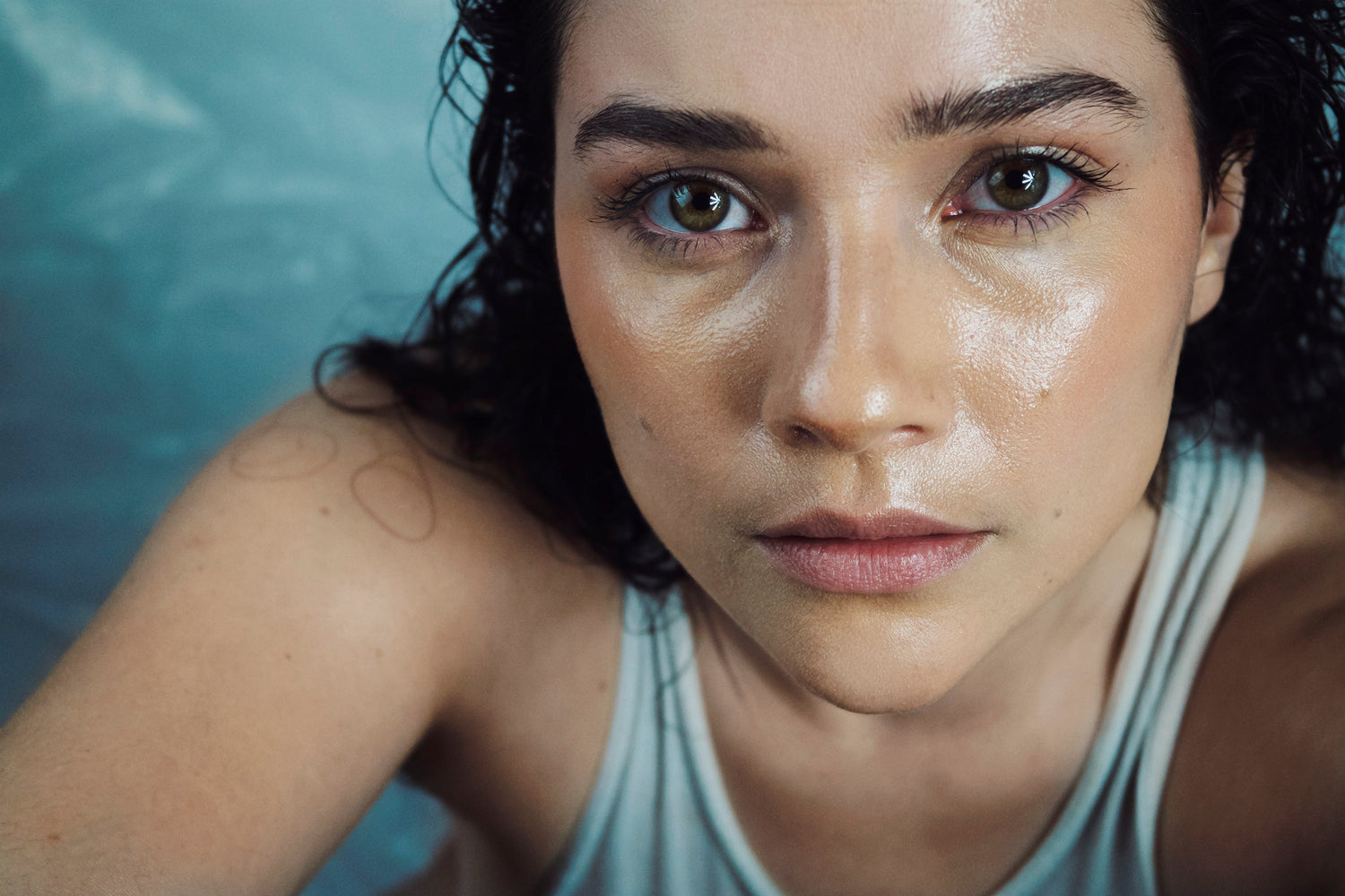 An intimate portrait of Xan shot from a high angle. Her dark hair is matted against her face and body. Her skin glows as she gazes intensely into the camera.