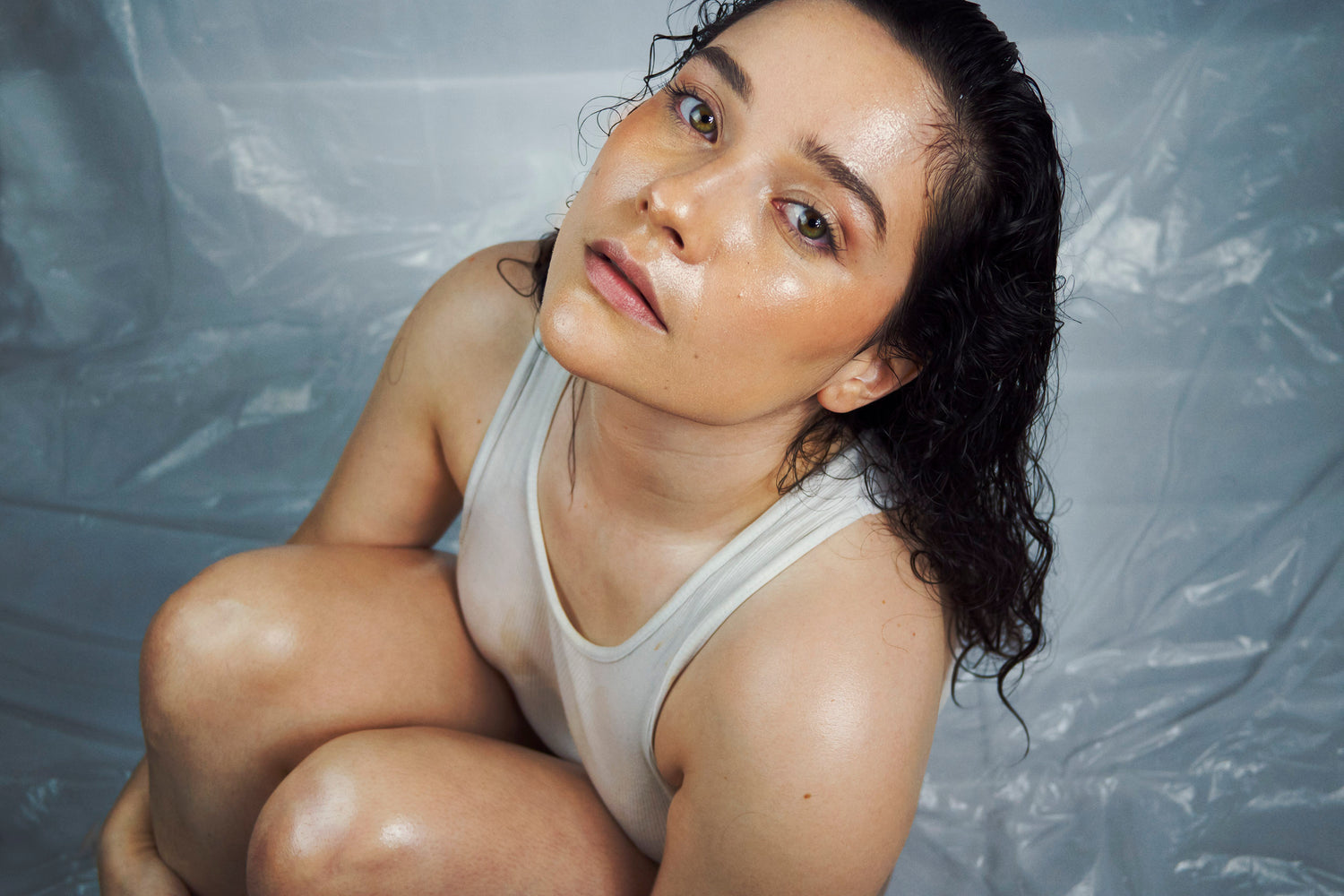 An intimate portrait of Xan shot from a high angle. Her dark hair is matted against her face and body. Her skin glows as she gazes intensely into the camera.